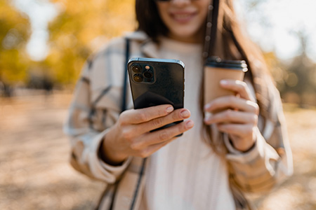 Someone holding both a coffee and a cell phone - she looks cold